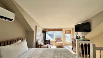 A bedroom with a bed, a chair, a desk with a TV, and a window with a view of buildings.