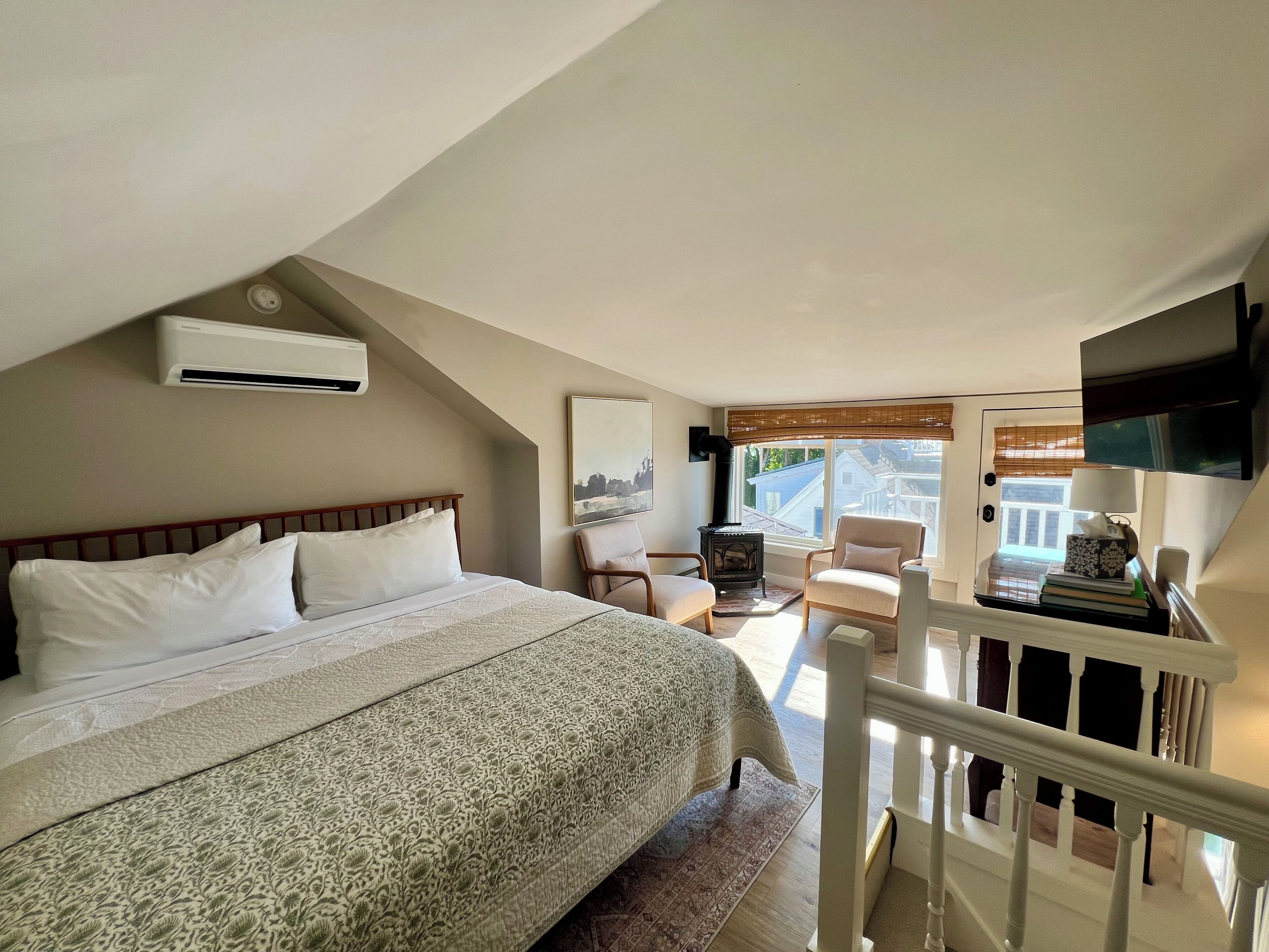 Un dormitorio con una cama grande, un televisor montado en la pared y una ventana con vistas al exterior.
