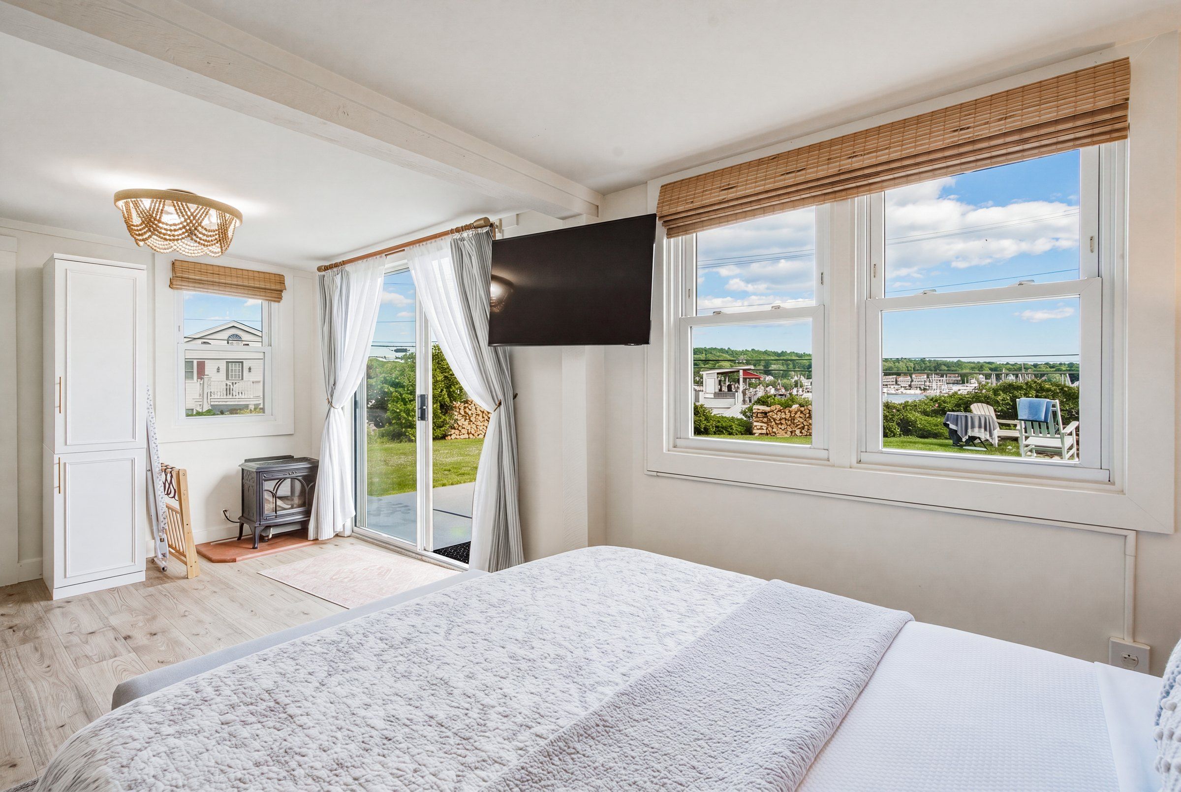 A bedroom with a bed, a television, a window with a view of the outside, and a door leading to another room.