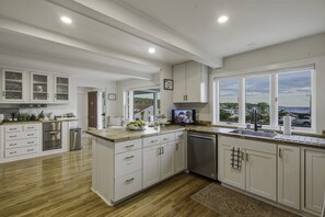 Una cocina moderna con armarios blancos, lavavajillas integrado y un amplio ventanal con vistas al mar.