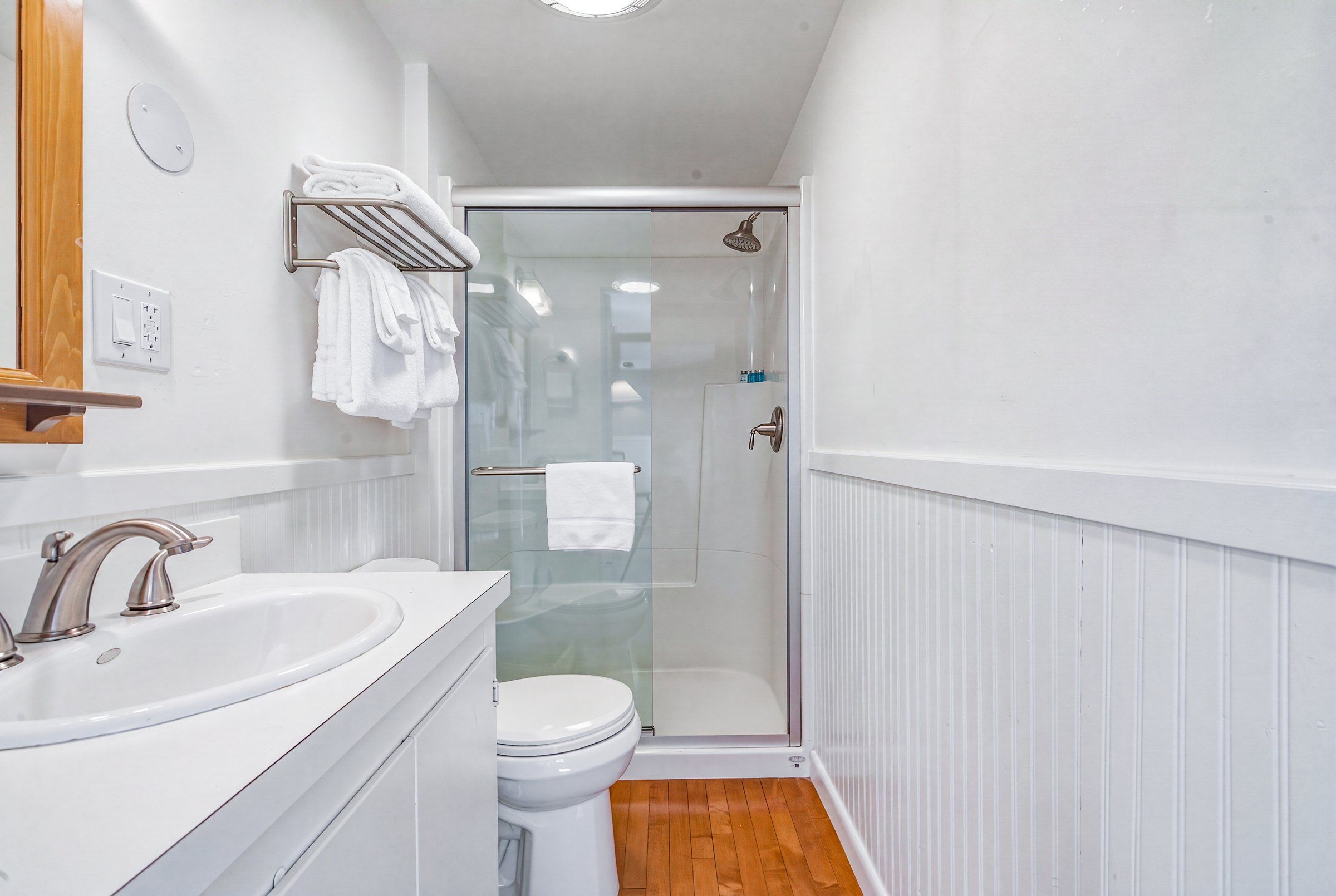 A bathroom with a white sink, a toilet, a glass shower enclosure, and a towel rack.