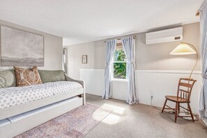 Une chambre à coucher avec un lit, une chaise, une fenêtre avec des rideaux, un radiateur et une lampe.