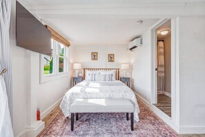 Un dormitorio con cama, mesitas de noche, ventana y aire acondicionado.