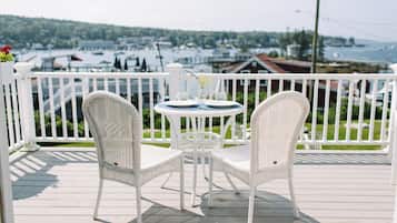 A white wicker table and chairs on a wooden deck with a view of a marina and buildings in the background.
