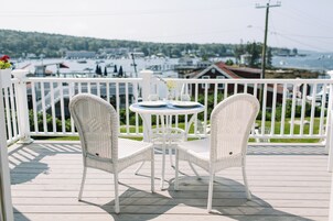 A white wicker table and chairs on a wooden deck with a view of a marina and buildings in the background.