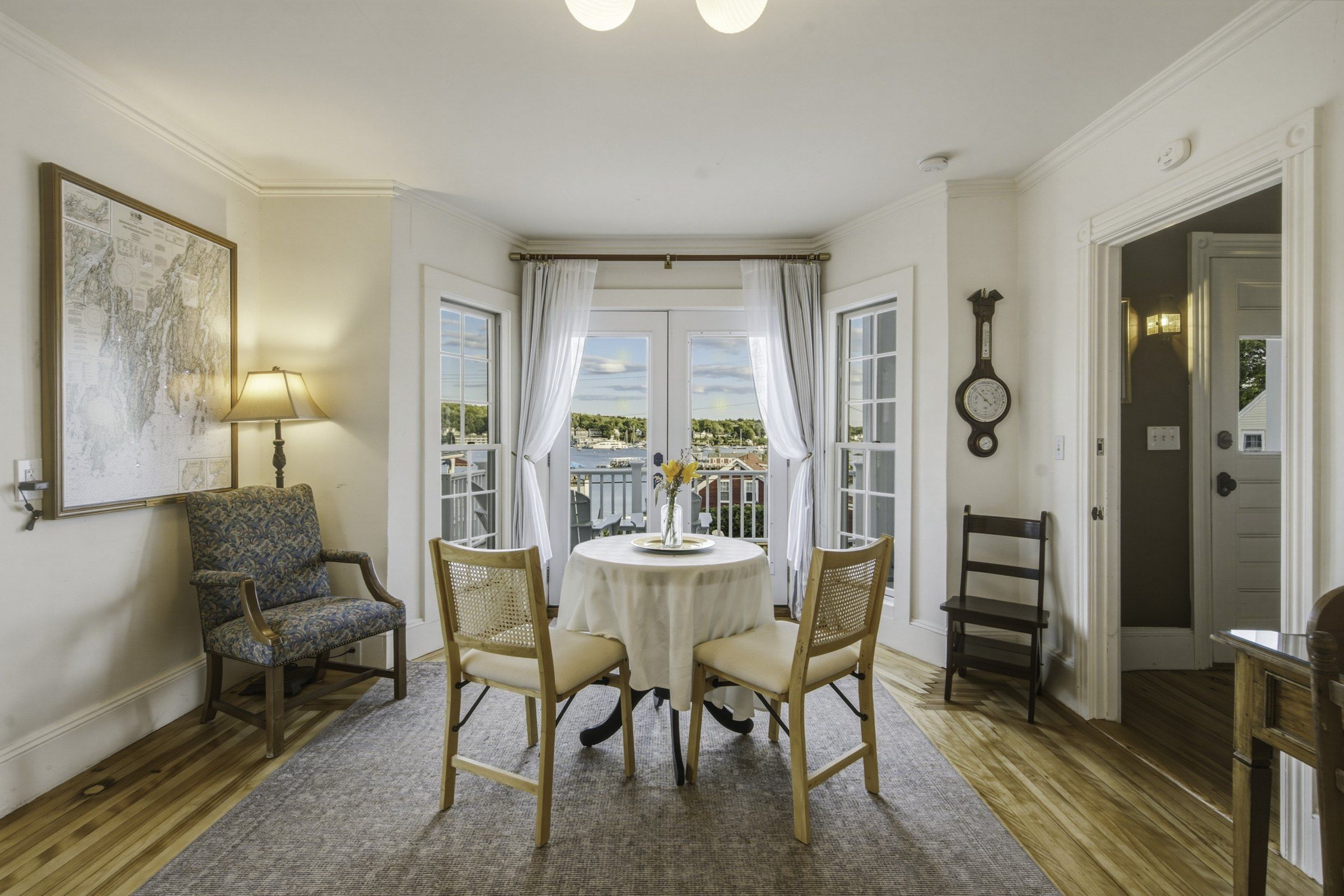A room with a round table, two chairs, a lamp, a wall clock, and a framed map.