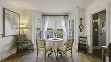A room with a round table, two chairs, a lamp, a wall clock, and a framed map.