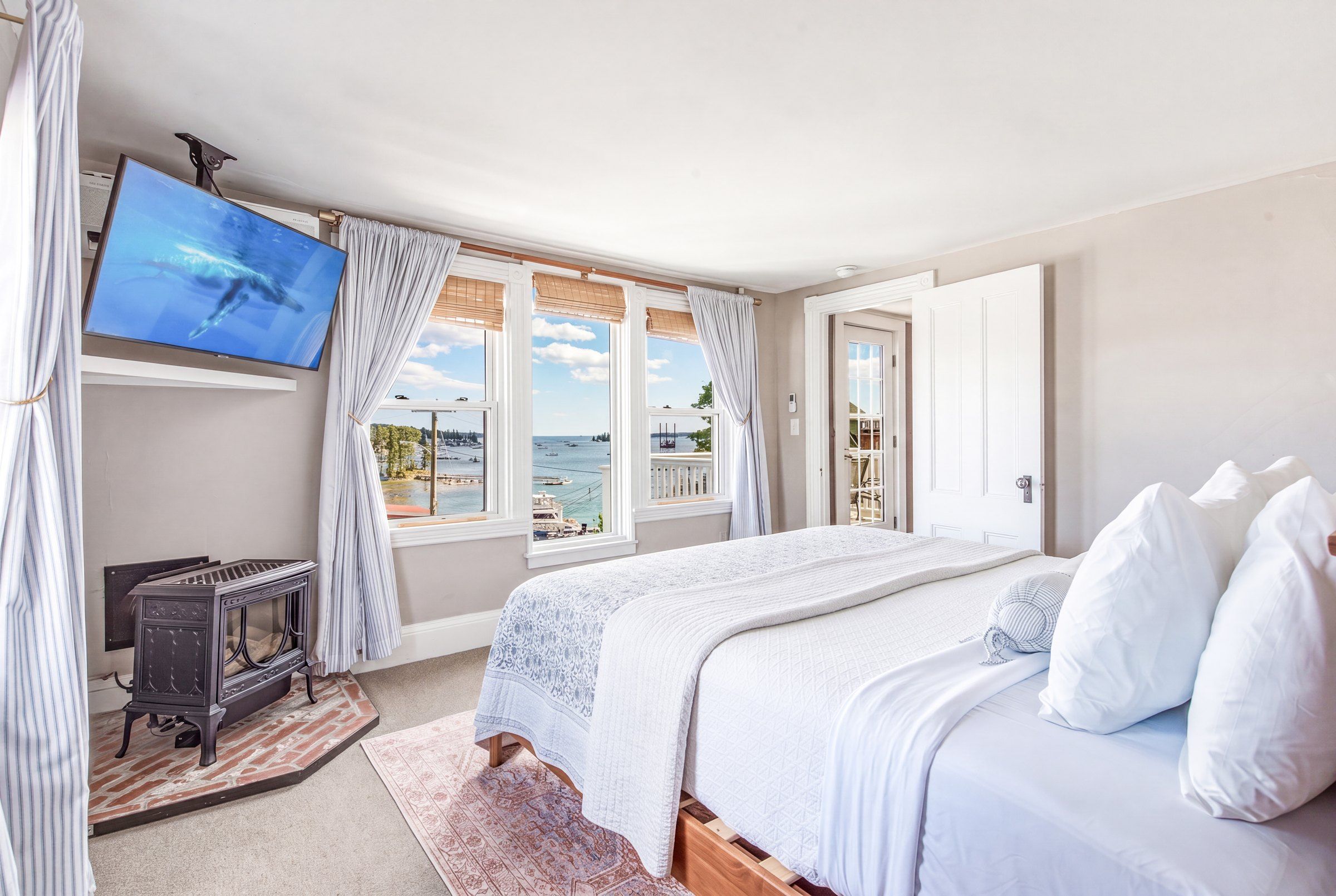 A bedroom with a bed, a television, a fireplace, and a view of the sea.