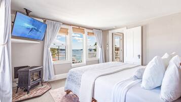 A bedroom with a bed, a television, a fireplace, and a view of the sea.