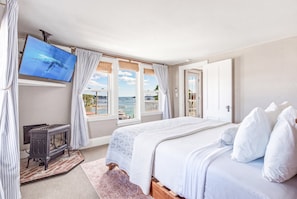 A bedroom with a bed, a television, a fireplace, and a view of the sea.