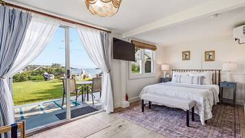 A bedroom with a bed, a TV, a window, and a view of the outdoors.