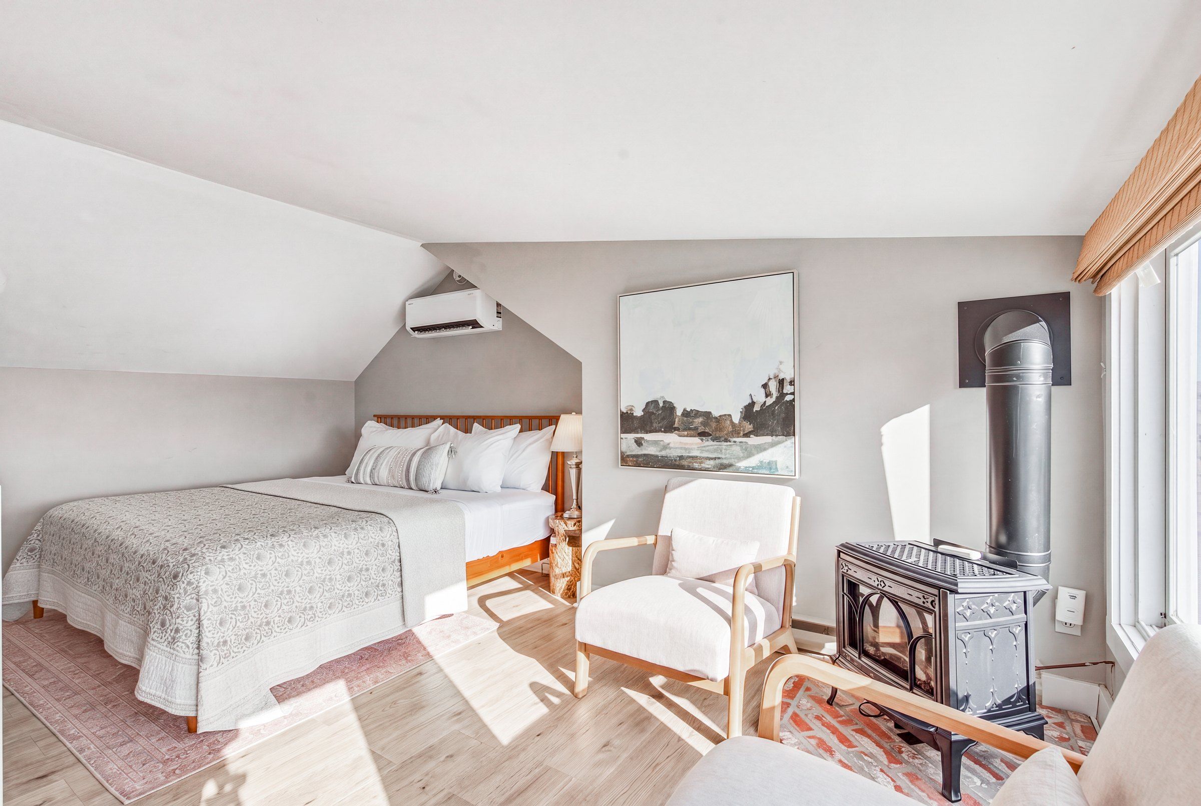 A bedroom with a bed, a chair, a fireplace, and a painting on the wall.