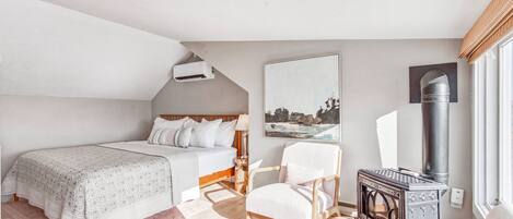 A bedroom with a bed, a chair, a fireplace, and a painting on the wall.