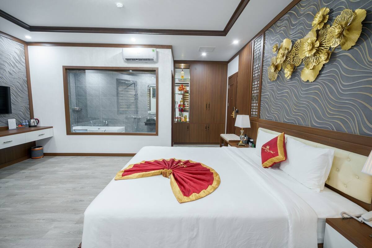 A hotel room with a large bed, a shower area, a vanity with a mirror, and a decorative wall panel.
