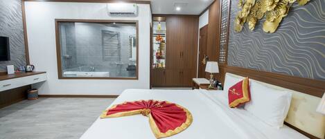 A hotel room with a large bed, a shower area, a vanity with a mirror, and a decorative wall panel.
