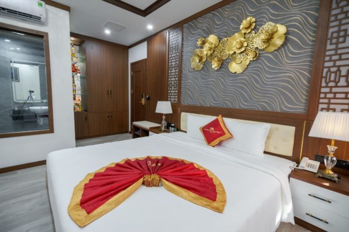 A hotel room with a neatly made bed, a wooden wardrobe, a bathroom with a mirror, and a decorative wall panel.