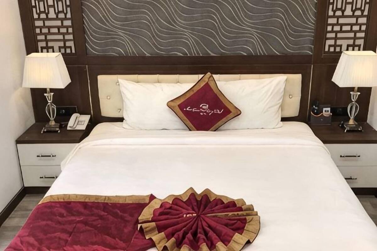 A hotel room with a large bed, two bedside tables with lamps, a decorative headboard, and a patterned wall.