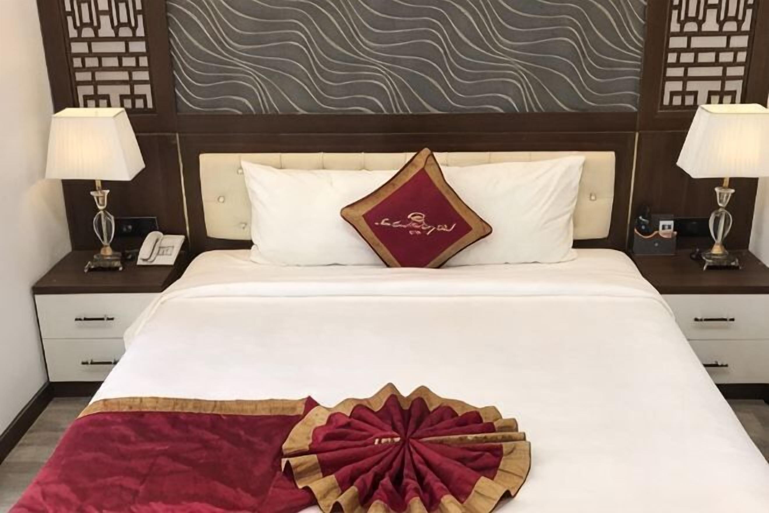 Ein Hotelzimmer mit einem großen Bett, zwei Nachttischen mit Lampen, einem Zierkissen und einer Wand mit Muster.