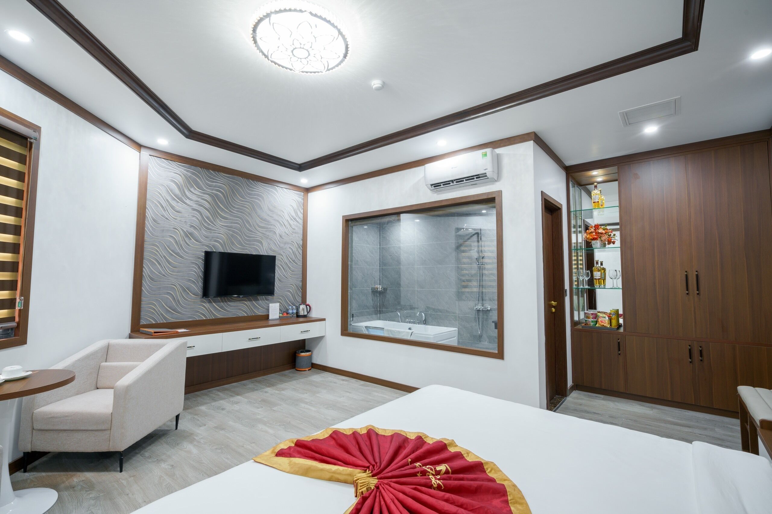 A modern hotel room with a large bed, a TV, a bathroom with a glass shower, and a wardrobe.