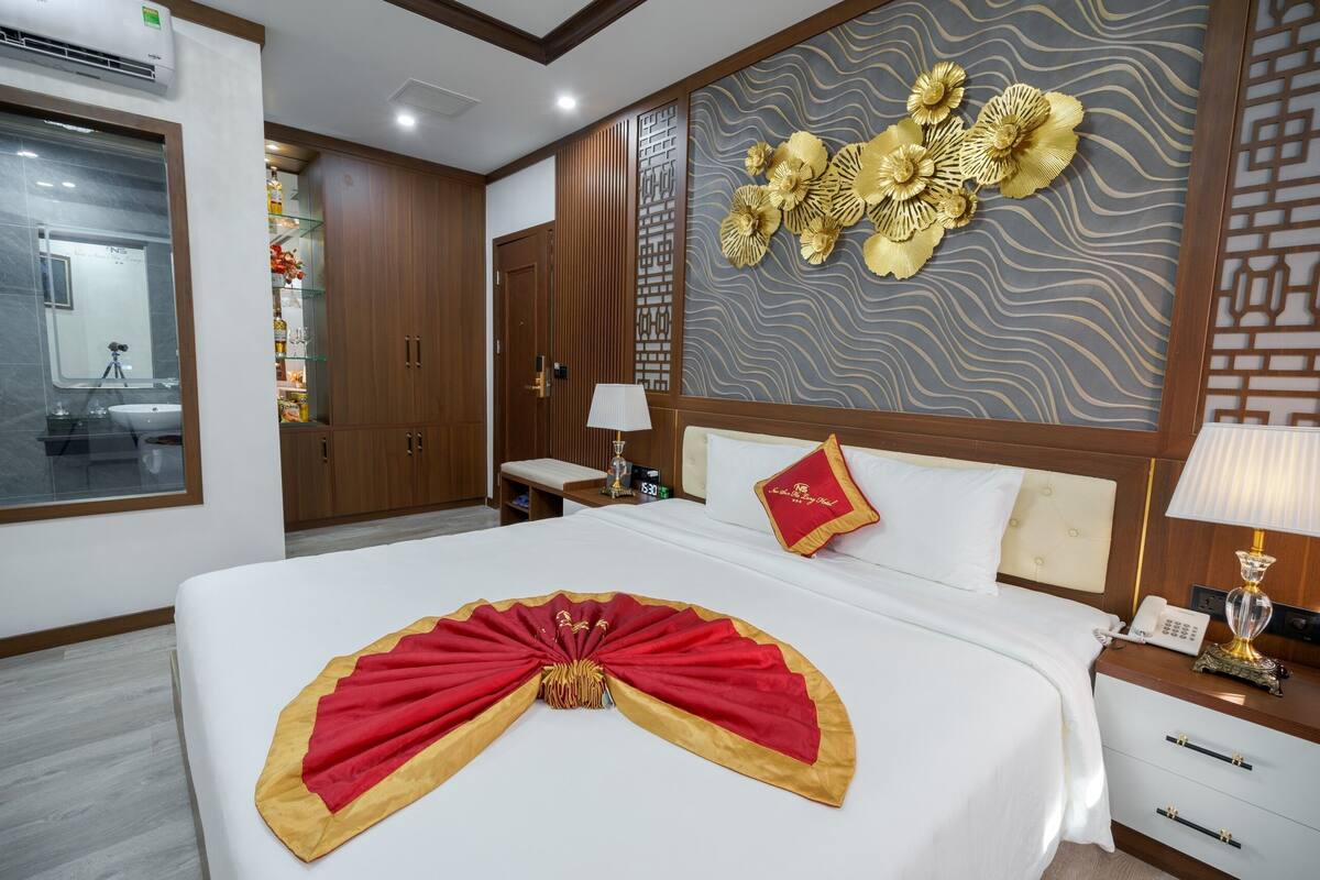 A hotel room with a large bed, a bedside table with a lamp, a wall with decorative panels, and a wardrobe.