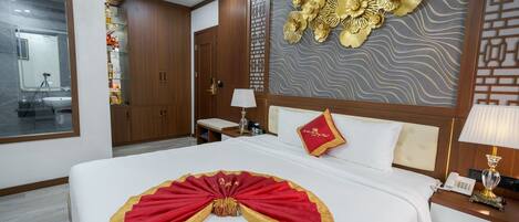 A hotel room with a large bed, a bedside table with a lamp, a wall with decorative panels, and a wardrobe.