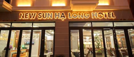 The exterior of the New Sun Ha Long Hotel with illuminated signage, large glass doors, and a reception area visible inside.