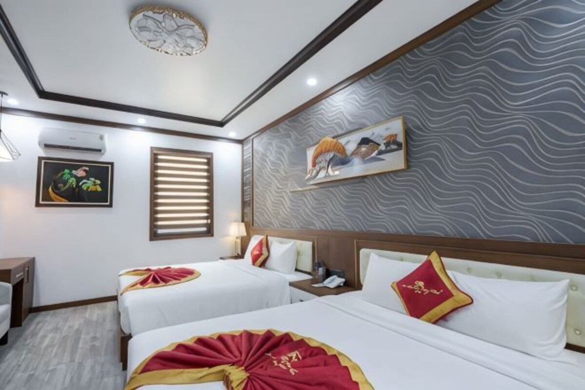 A hotel room with two beds, a wooden headboard, a wall-mounted artwork, and a ceiling light fixture.