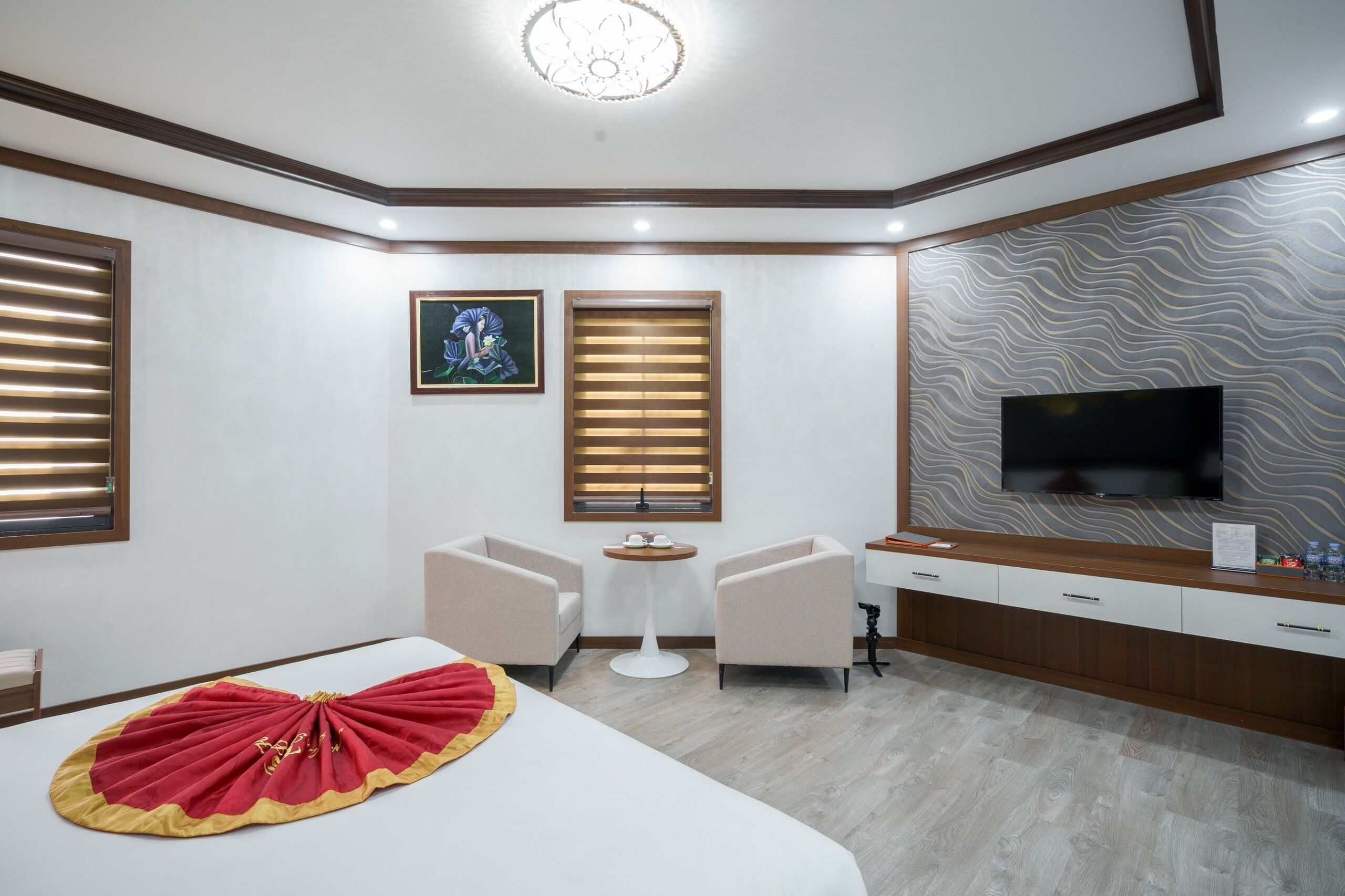 A hotel room with a bed, two armchairs, a small table, a TV, and a wooden cabinet.