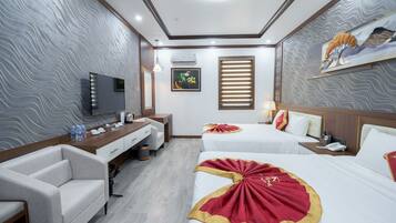 A hotel room with a modern design, featuring two beds with red and gold bedding, a flat-screen TV, a desk with a chair, and a small seating area.