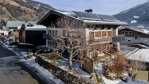 A modern chalet with a sloped roof, solar panels, and a view of snow-covered mountains.