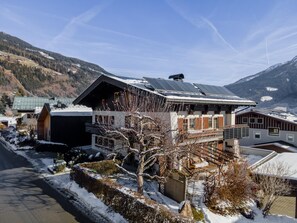 A modern chalet with a sloped roof, solar panels, and a view of snow-covered mountains.
