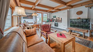 A cozy living room with a leather sofa, wooden coffee table, and a dining area with a bench. A kitchen with white cabinets and a green cabinet is visible.
