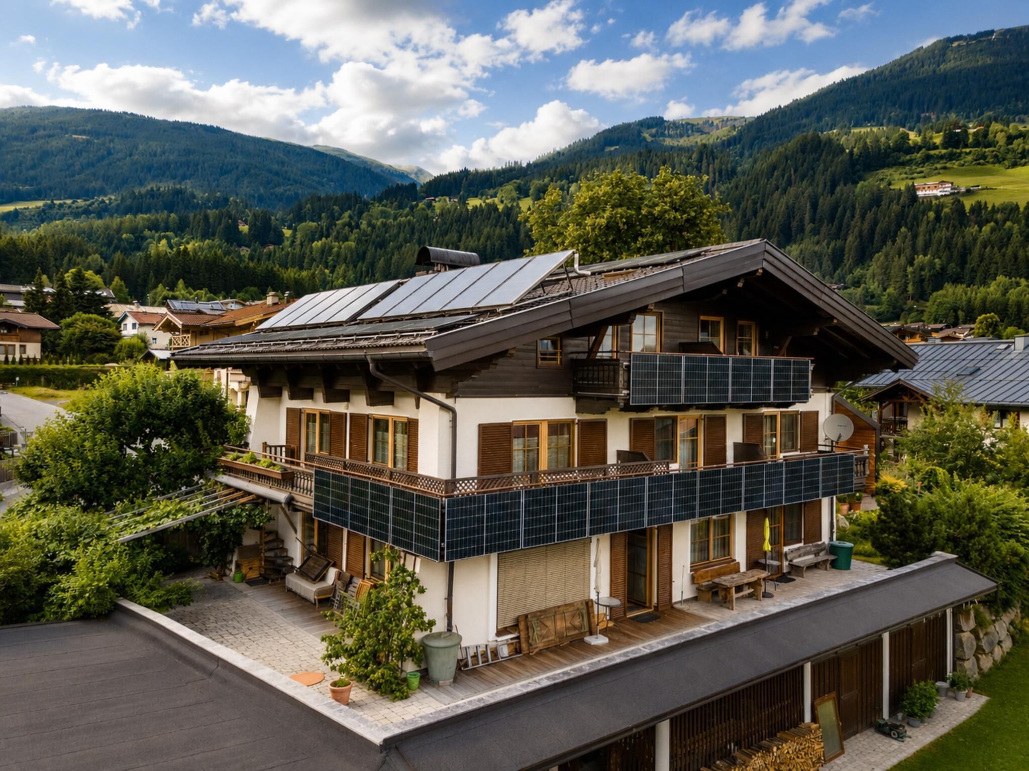 A modern two-story house with a balcony, solar panels, and a view of the surrounding mountains.