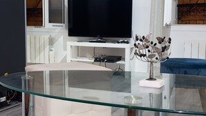 Un soggiorno moderno con un tavolino da caffè in vetro, una TV a schermo piatto su un mobile bianco e una scultura decorativa in metallo.