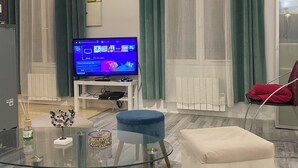 Un soggiorno moderno con un tavolino in vetro, un divano bianco, una poltrona rossa e un televisore a schermo piatto su un mobile bianco.