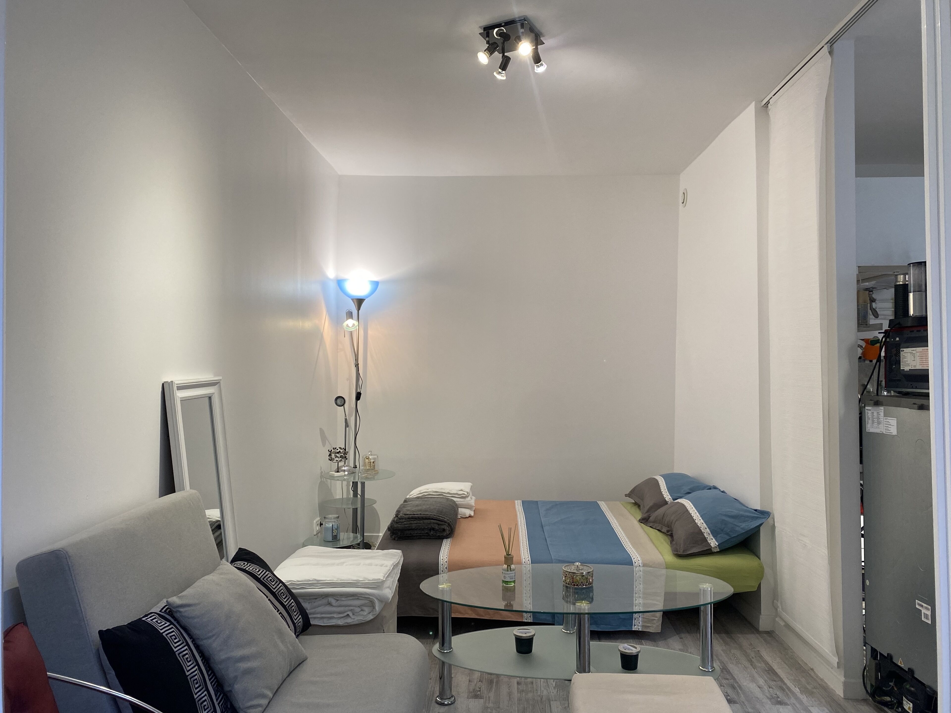Ein kleines Hotelzimmer mit Bett, Glastisch, Schlafsofa und Nachttischlampe.