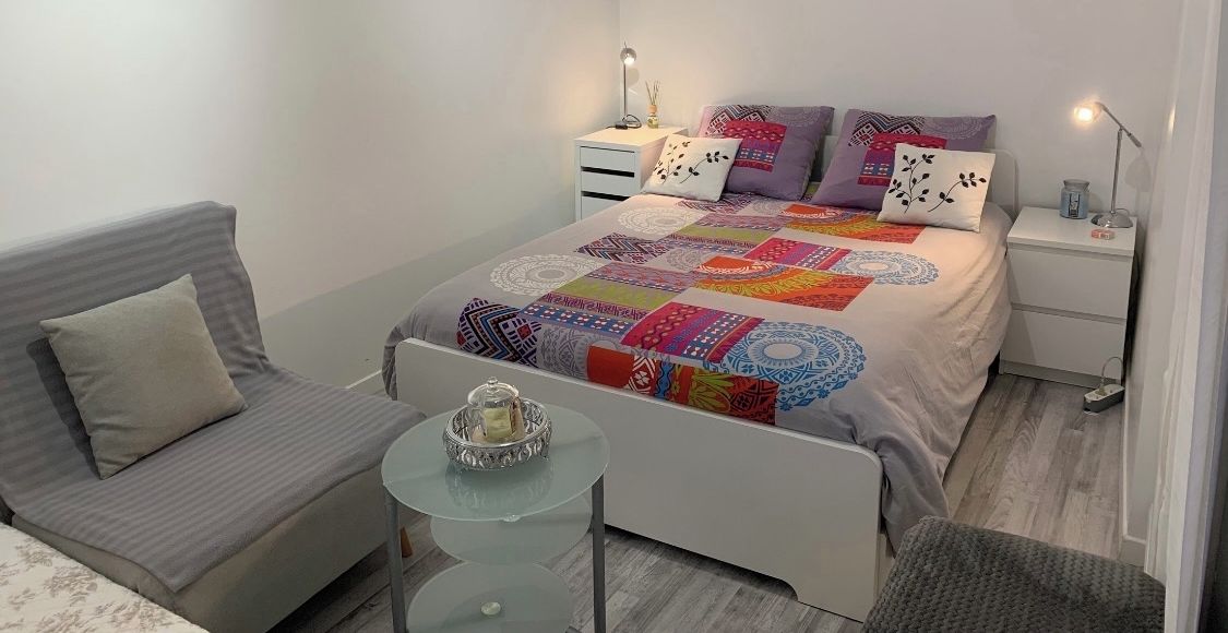 Ein modernes Schlafzimmer mit einem Bett, Nachttischen, einem kleinen runden Tisch und einer Couch.