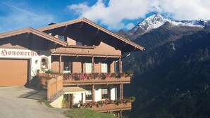 A chalet-style building with a wooden facade, a balcony with flowers, and a mountain backdrop. - Beautiful apartment in a dream location in Finkenberg (Finkenberg)