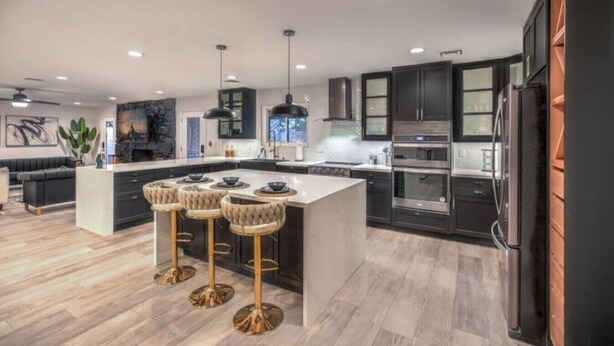 A modern kitchen with dark cabinetry, stainless steel appliances, a central island with bar stools, and a large island with a built-in oven.