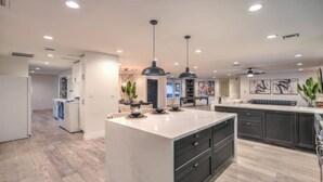 A modern kitchen with a large island, pendant lighting, and a dining area with a pool table.