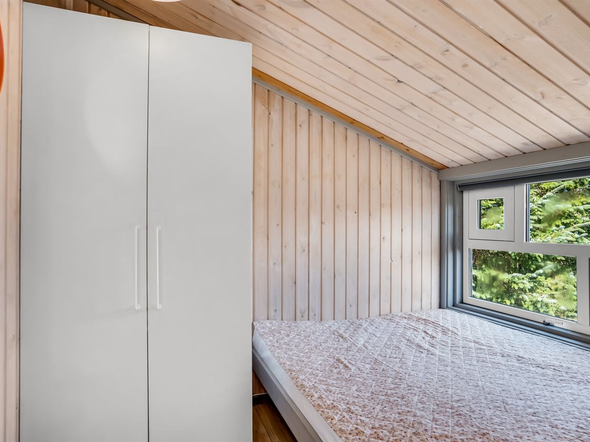 Quarto com cama, guarda-roupa e janela com vista para o verde.