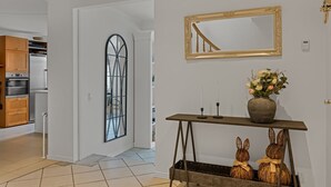 Ein modernes Interieur mit einer Küche, einem dekorativen Spiegel, einem Konsolentisch mit Kerzen und einer Vase mit Blumen.