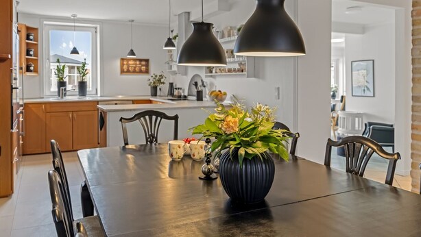 Eine moderne Küche mit Pendelleuchten, einem Esstisch mit Stühlen und einer Blumenvase.