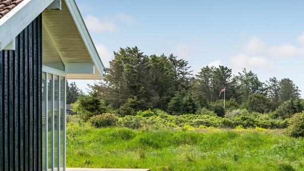 Een modern gebouw met een houten terras en grote ramen met uitzicht op een weelderig groen landschap.