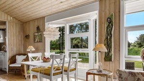 Een modern interieur met een eethoek, witte meubels en grote ramen met uitzicht op groen.