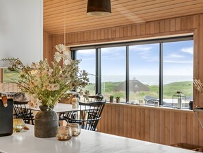 Un coin repas avec une grande fenêtre, un plafond en bois et un vase rempli de fleurs sur la table.