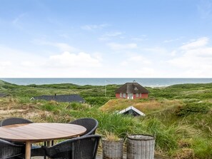 Une propriété située sur la côte, avec un espace repas agrémenté de meubles en osier et d’une table, une maison rouge avec un toit de chaume et une vue sur la mer.