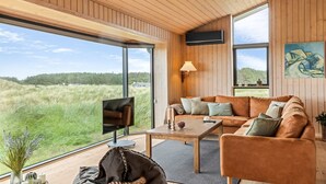 A modern interior with a wooden ceiling, large windows, a sofa, a coffee table, and a television.