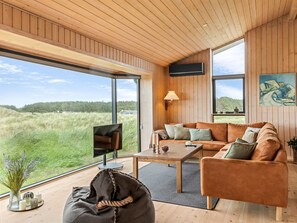 Un intérieur moderne avec un plafond en bois, de grandes fenêtres, un canapé, une table basse et un téléviseur.
