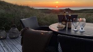 A table set for two with a bottle of beer and glasses, overlooking a sunset over the sea.